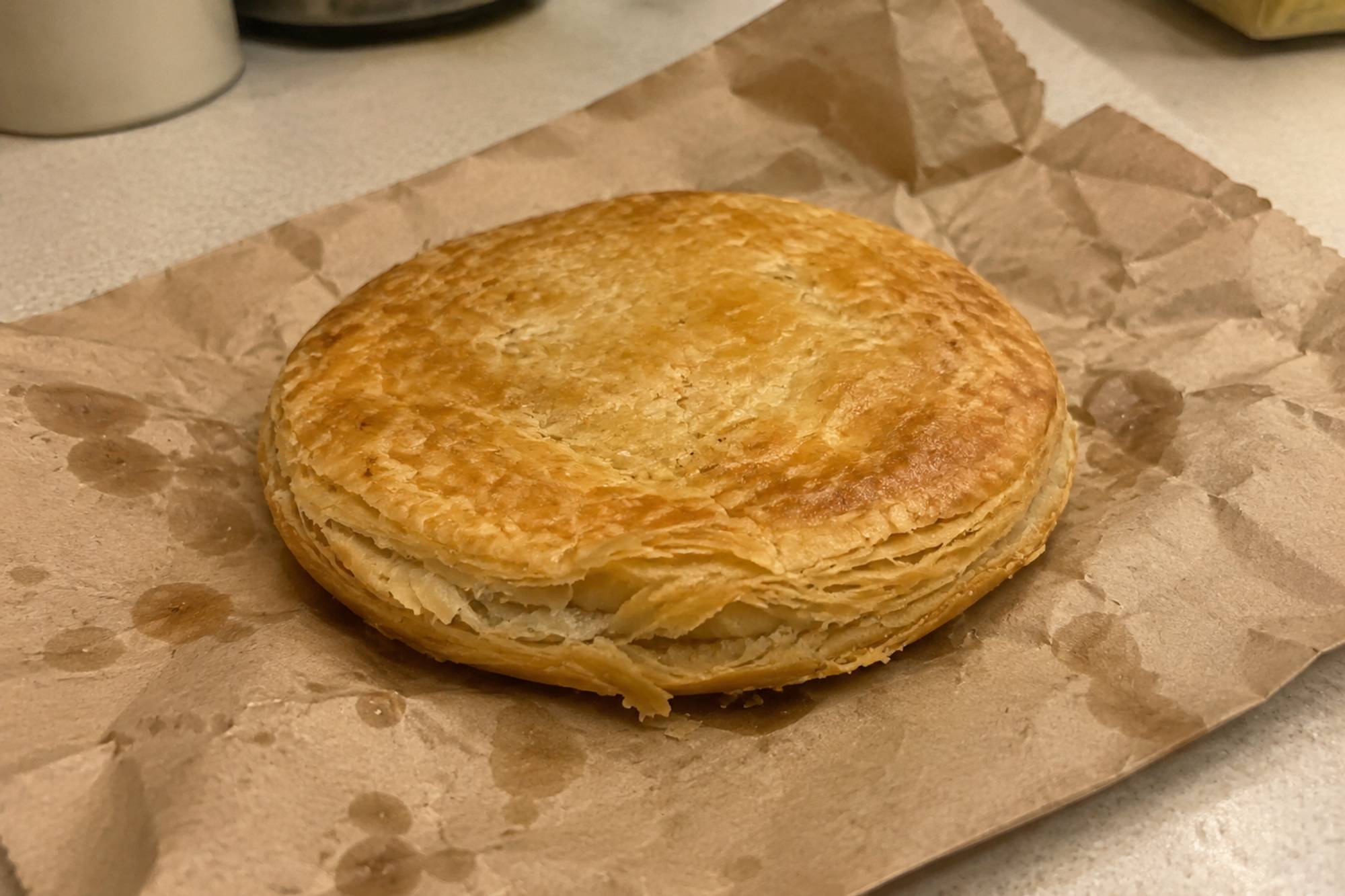 A flat round golden puff pastry chicken pie on paper